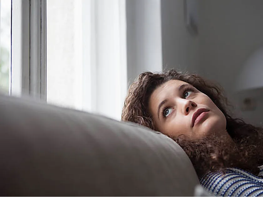 Frau liegt auf dem Sofa und schaut mit nachdenklichem Blick nach oben.